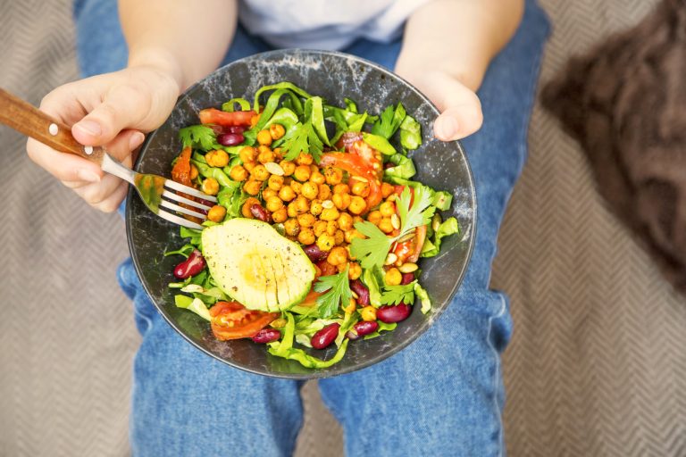 A person in blue jeans holding a healthy plate of food