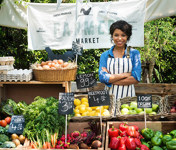 A woman selling at a farmers market. There are many farm produce on display.