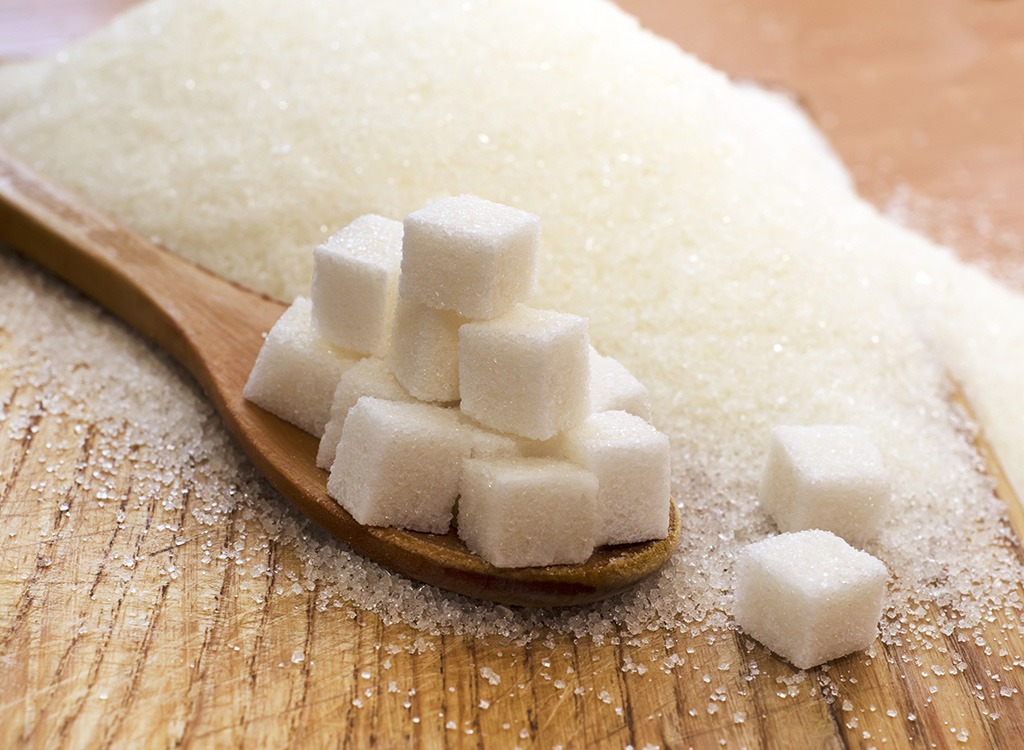 Cubes of sugar in a wooden spoon. On the background is a heap of sugar: too much sugar